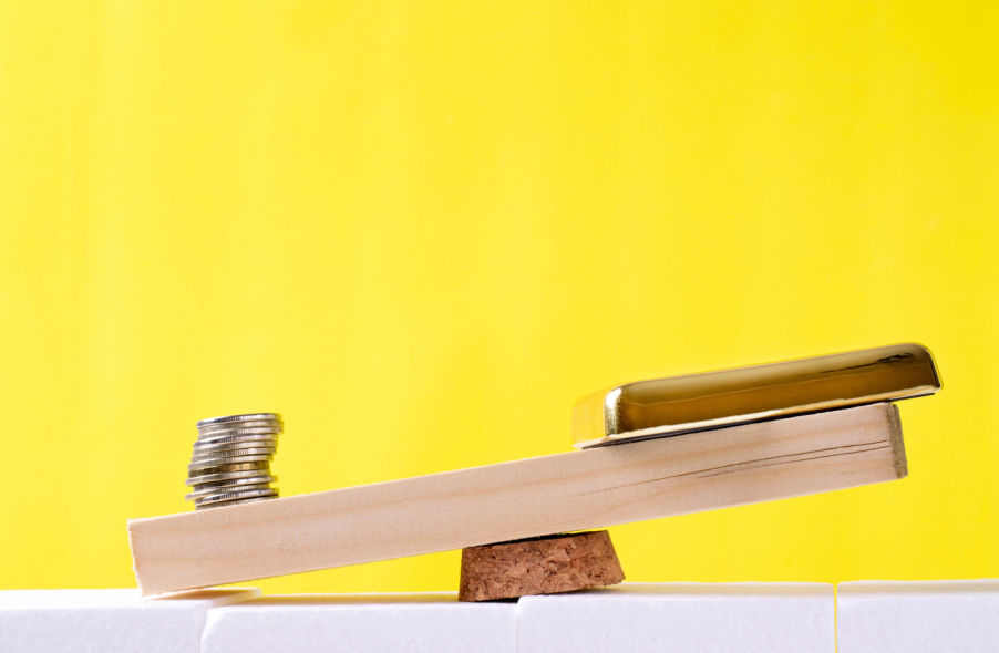 stack of coins outweighing gold bar on scale on yellow background