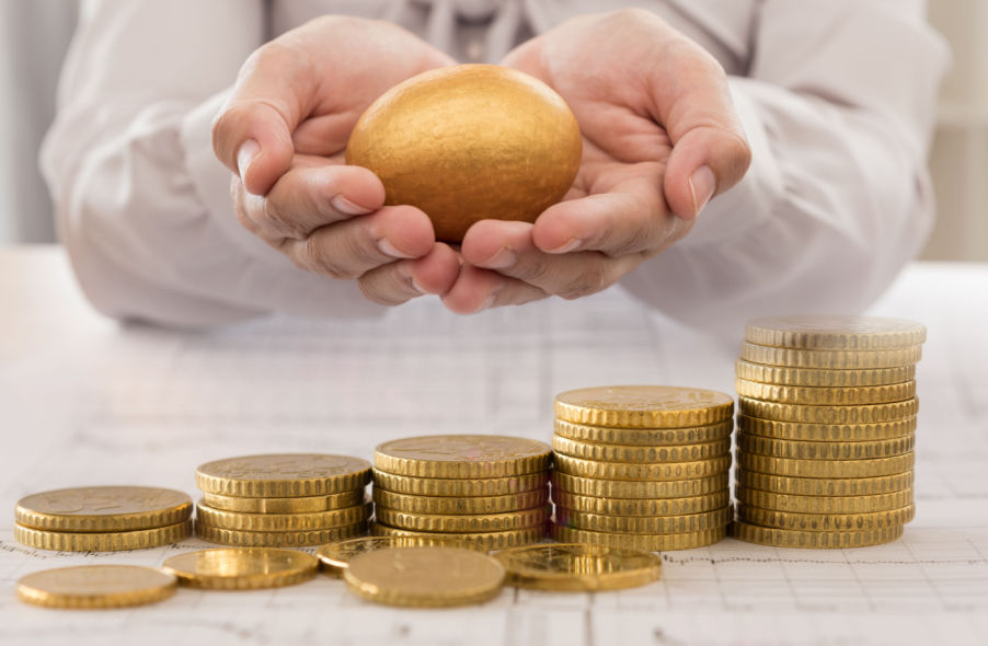 hand holding gold egg and stack of gold coins