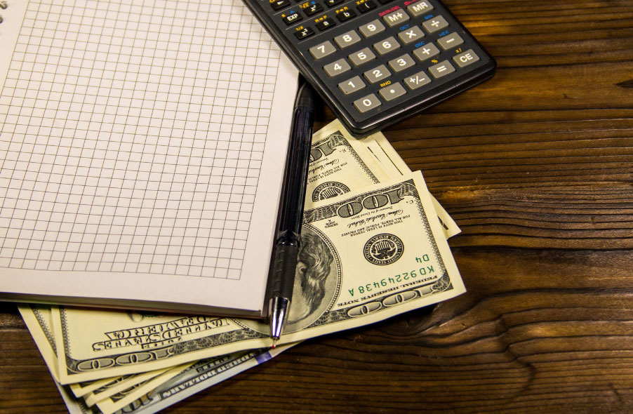 notebook pen calculator and dollar bills on wooden desk